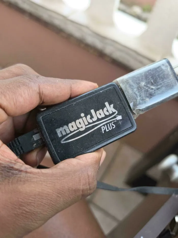 A hand holding a black magicJack Plus, a piece of vintage tech used for making phone calls over the internet.