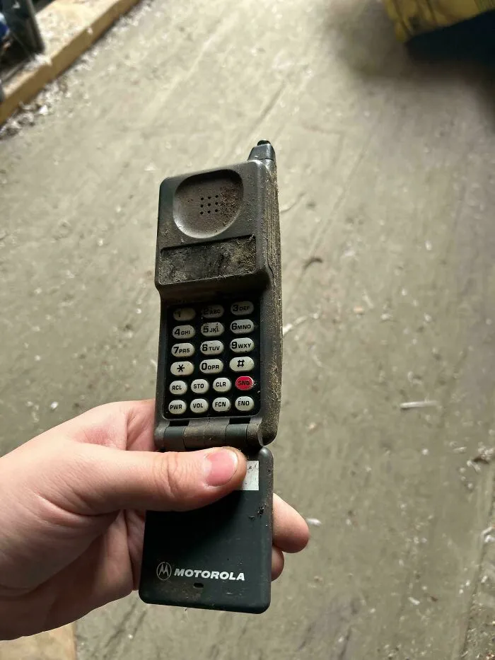 Hand holding a dusty Motorola flip phone, a classic example of vintage tech with physical buttons.