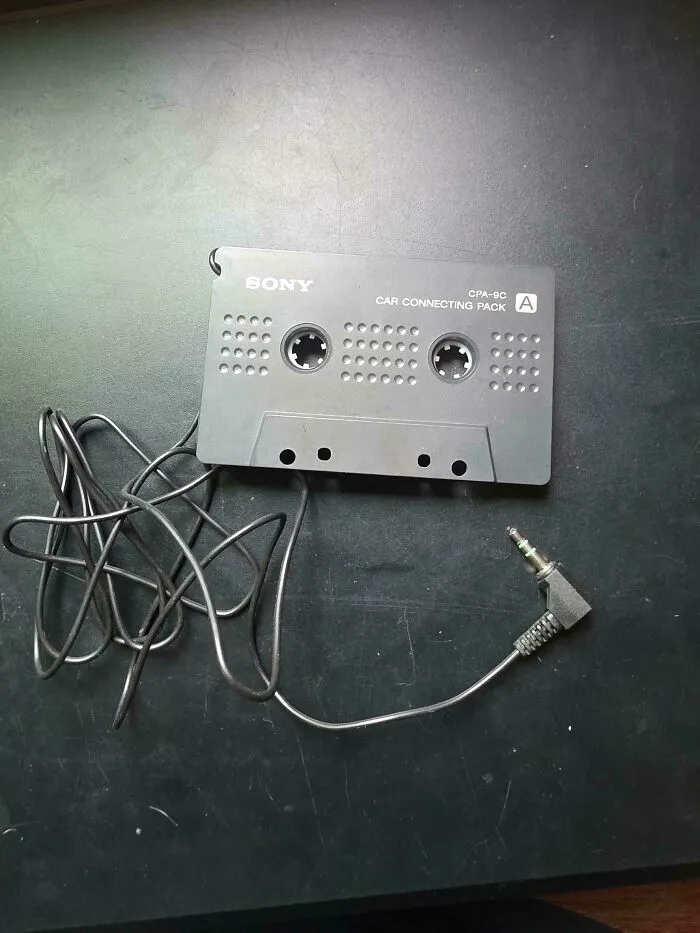 Vintage tech Sony cassette adapter with auxiliary cord on dark surface