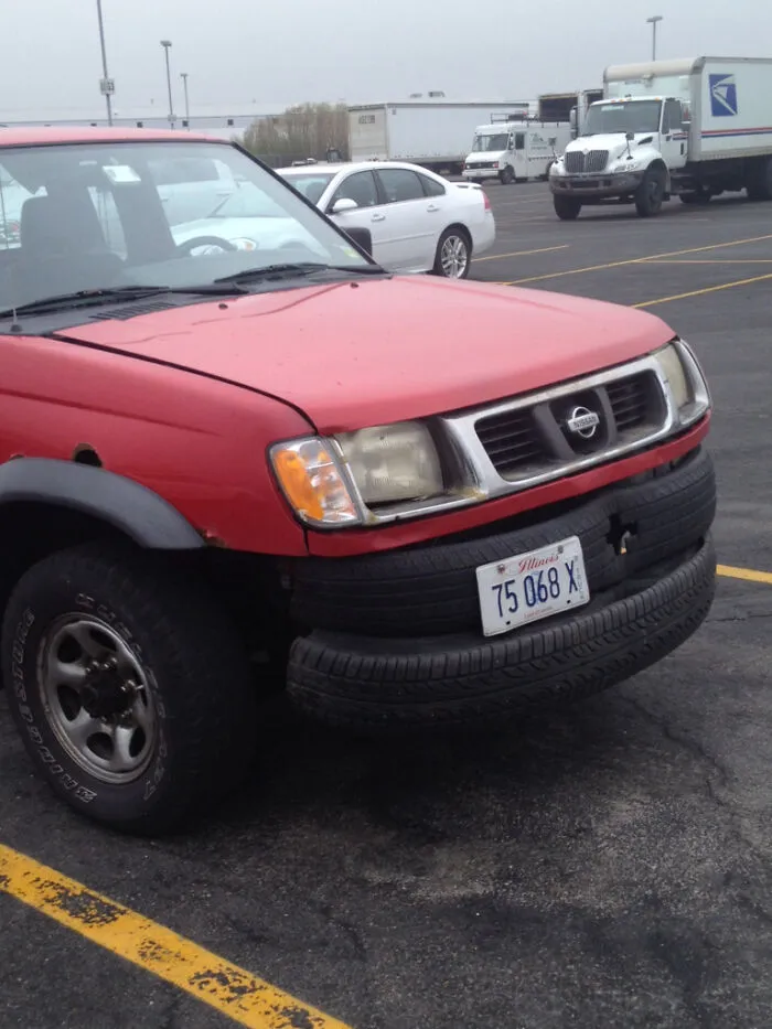 Redneck fixes featuring a red pickup truck with old tires used as a front bumper.