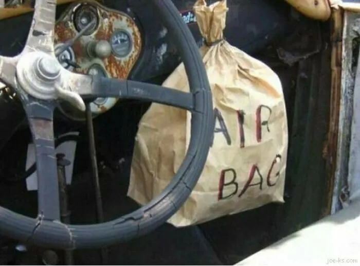 A paper bag labeled AIR BAG tied to a steering wheel showing redneck fixes