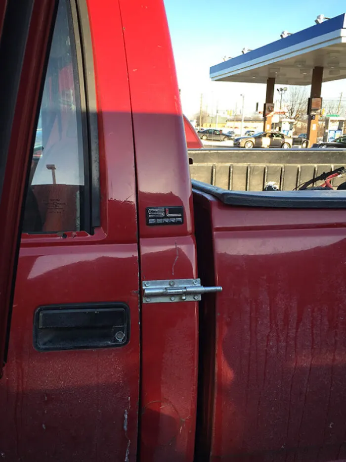 A red pickup truck door secured with a home door latch bolt as a funny redneck fix.