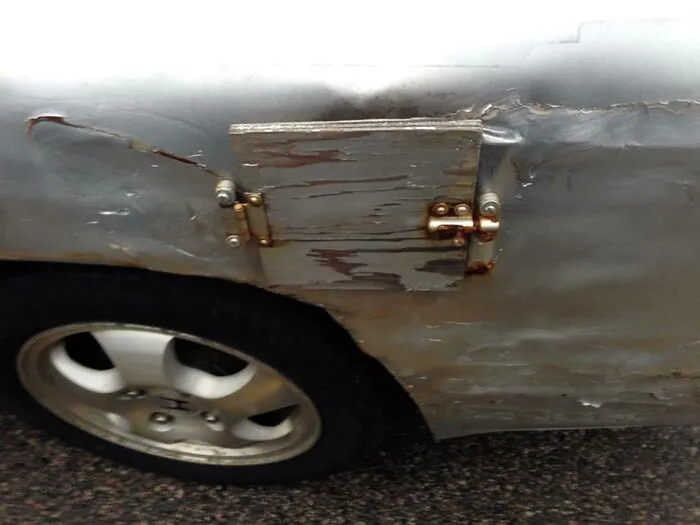 A car fuel door replaced with wooden board and latch as one of the redneck fixes.