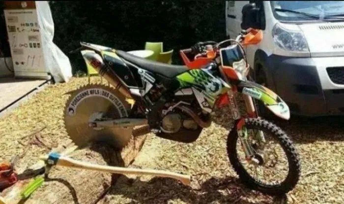 A dirt bike with a circular saw blade back wheel showing creative redneck fixes.