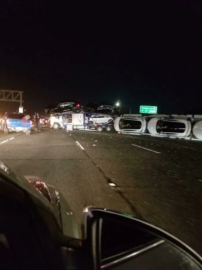 An overturned car carrier truck on a highway at night, showing expensive accidents