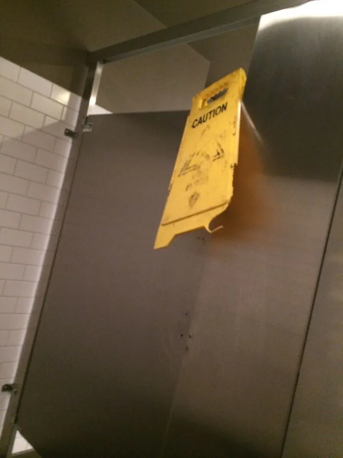 A yellow wet floor caution sign used as a door latch in a redneck fix