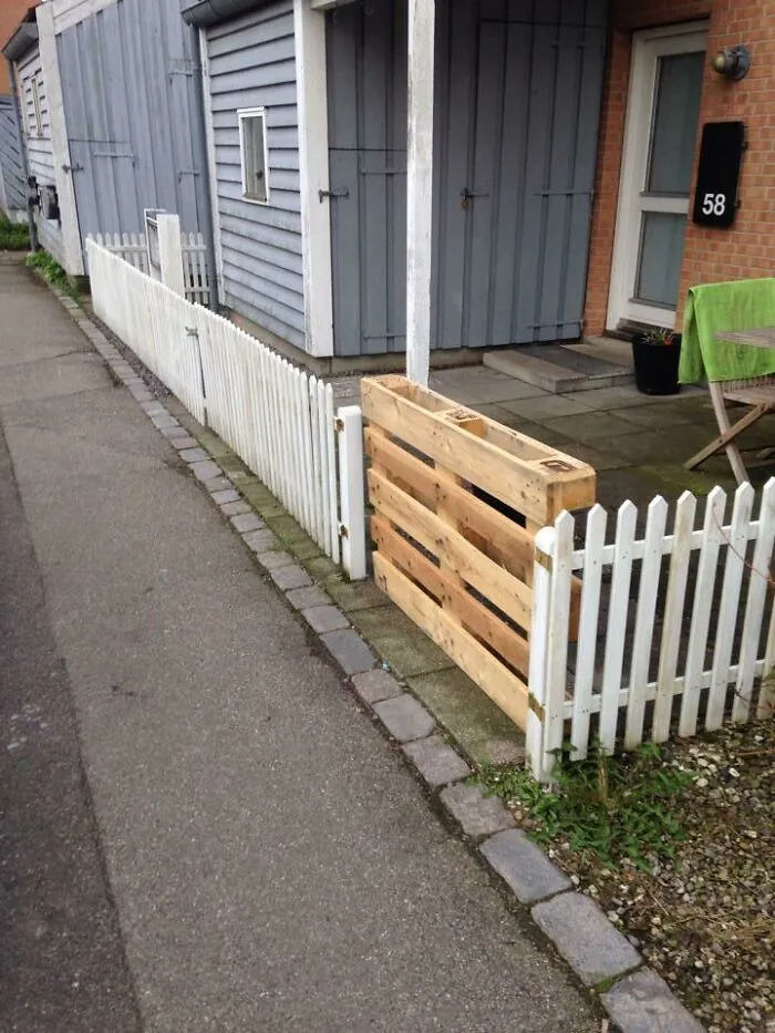 A wooden pallet used as a gate in a white picket fence, showcasing a clever redneck fix.