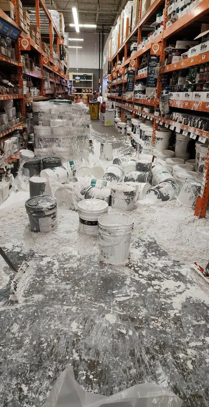 Spilled white paint completely covering the floor of a hardware store aisle, showing expensive accidents
