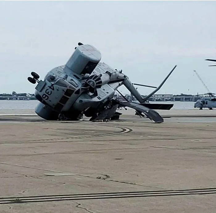 A military helicopter tipped over on its side on a runway, showcasing one of many expensive accidents