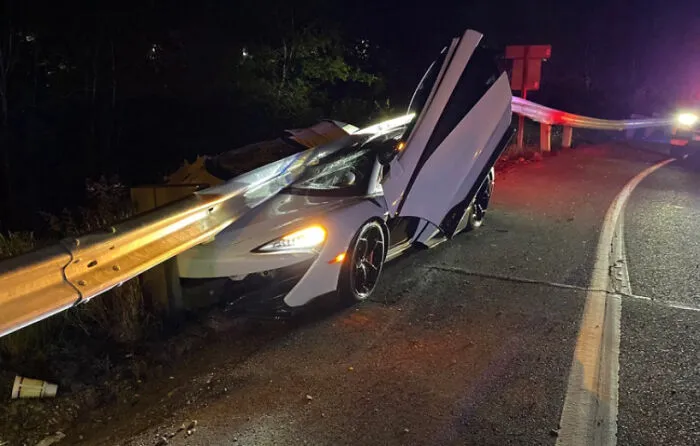 A white luxury sports car crashed underneath a highway metal guardrail, representing expensive accidents