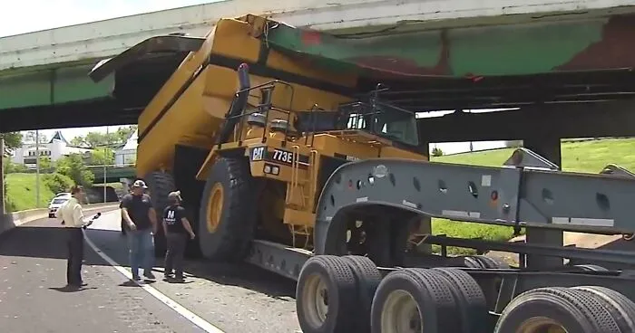 A large yellow dump truck stuck under a low bridge, showing expensive accidents.