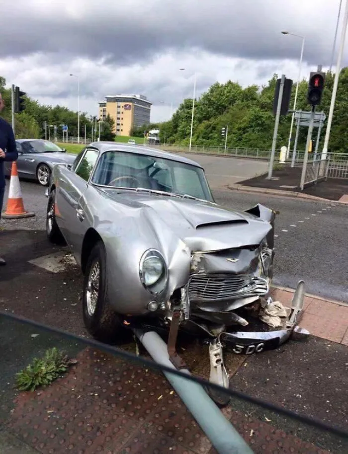 A silver vintage sports car severely damaged on the road, illustrating expensive accidents