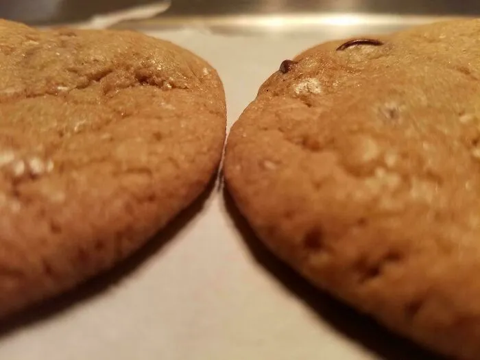 Satisfying close-up of two perfectly baked golden-brown cookies sitting next to each other on parchment paper.