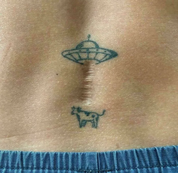 UFO tattoo integrated with a vertical back scar beam lifting a small cow, illustrating clever ideas