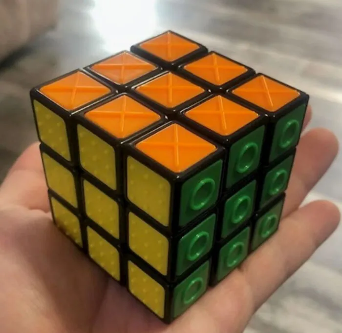 A hand holding a tactile Rubik cube with textured surfaces designed as clever ideas for blind players