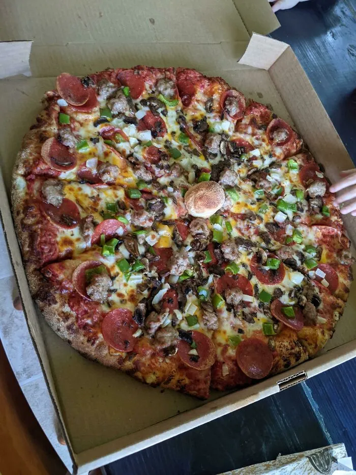 Large fresh pizza in box with a small dough ball in middle as a clever idea
