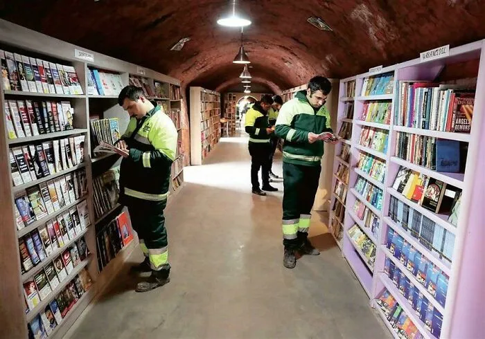 Sanitation workers in high-vis jackets read books in a cozy library, showcasing clever ideas.