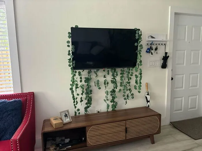 Wall-mounted television draped with fake vines displaying failed interior design choices around media console