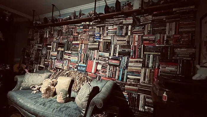 Massive home bookshelf wall filled completely with books behind a cozy sofa.