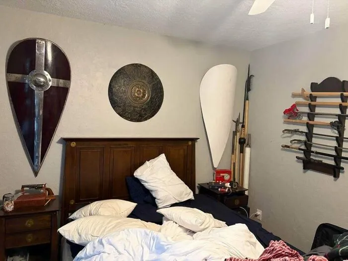 Questionable interior design choice showing a bedroom decorated with shields, swords, and polearms on the wall