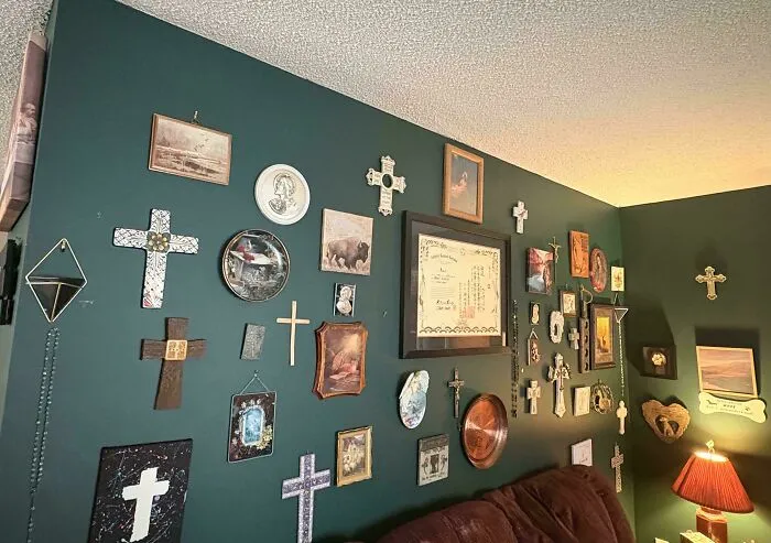 Cluttered interior design with dozens of crosses, frames, and wall decor items crowded on a green accent wall