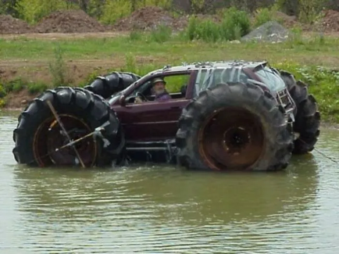 A sedan modified with giant tractor wheels floating in water, demonstrating extreme redneck fixes.