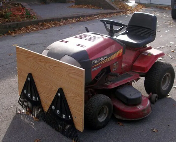 A red lawn mower fitted with a wooden board and rakes as a snowplow attachment, illustrating redneck fixes.