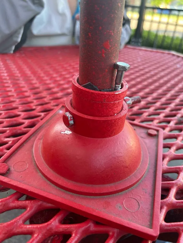 A red outdoor table umbrella base secured tightly using metal bolts, showcasing creative redneck fixes.