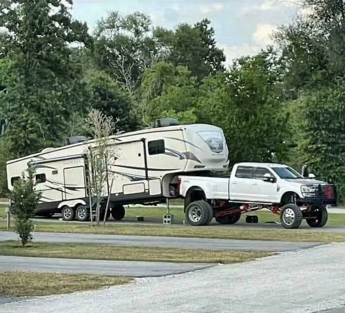 Lifted white pickup truck towing a large travel trailer as part of genius redneck fixes.
