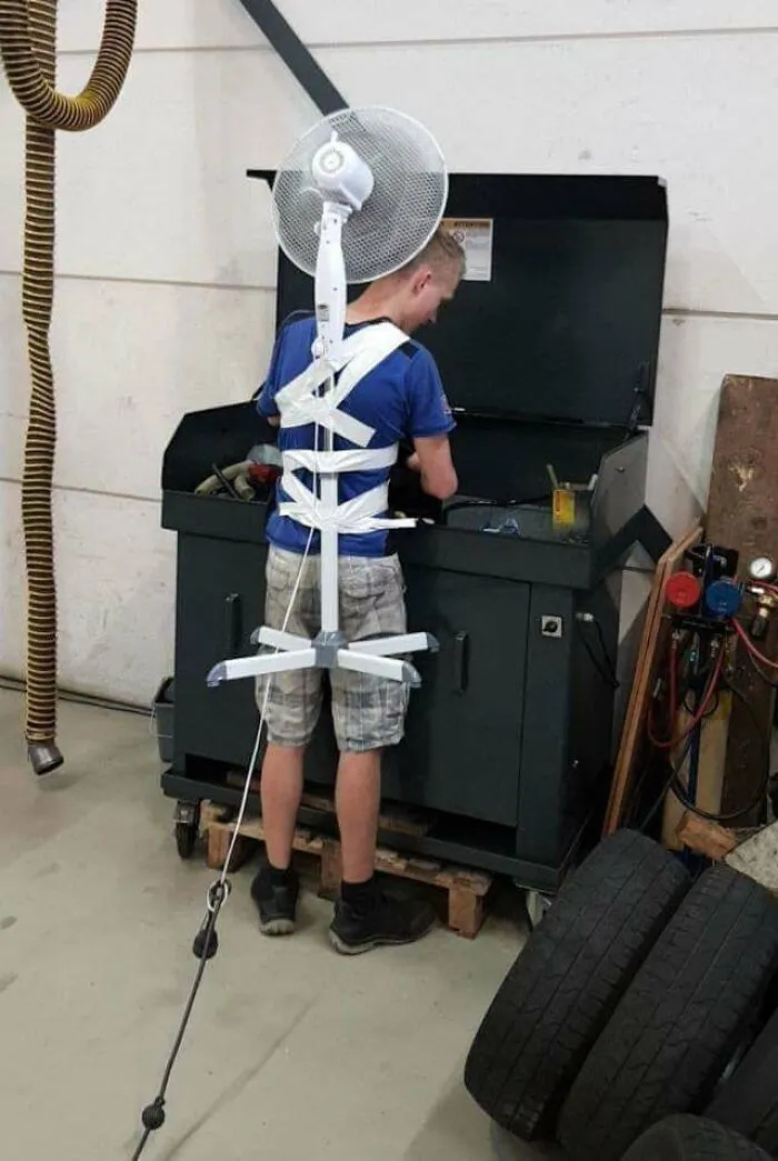 A man wearing a standing fan strapped to his back for creative redneck fixes.