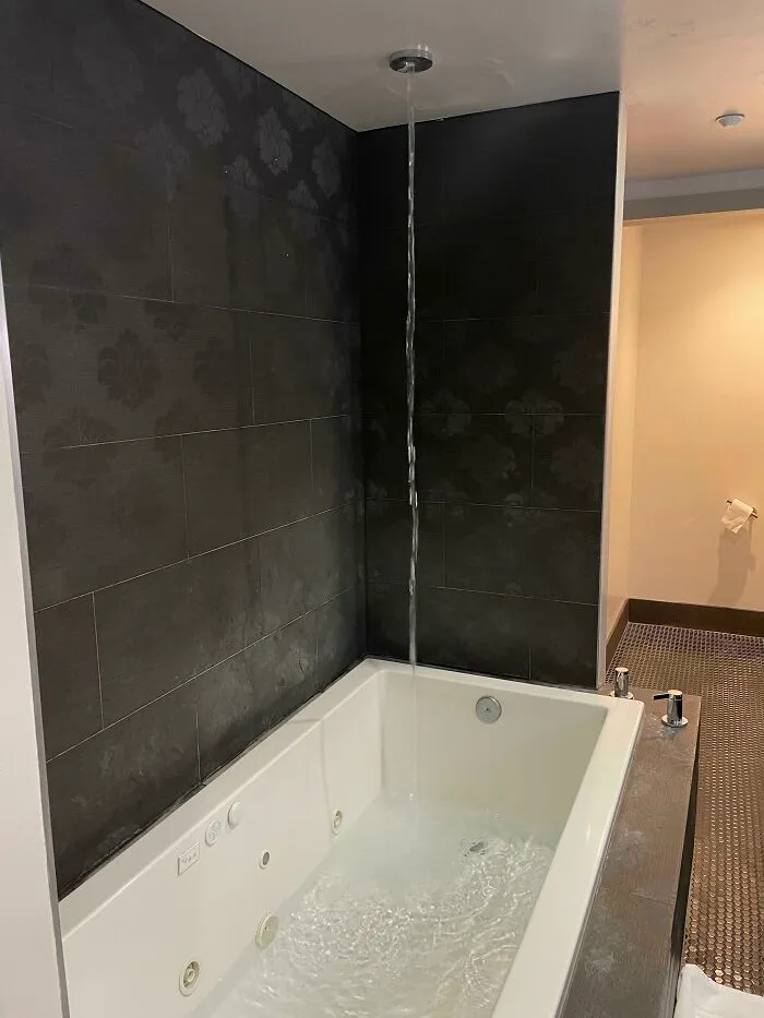 Questionable interior design decision showing a high ceiling shower head pouring water directly into a bathtub