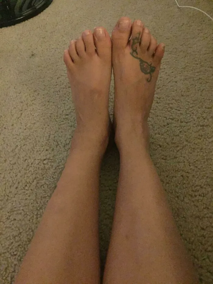 Top-down view of bare legs and feet with a tattoo, highlighting unusual foot structure and human anatomy variations.
