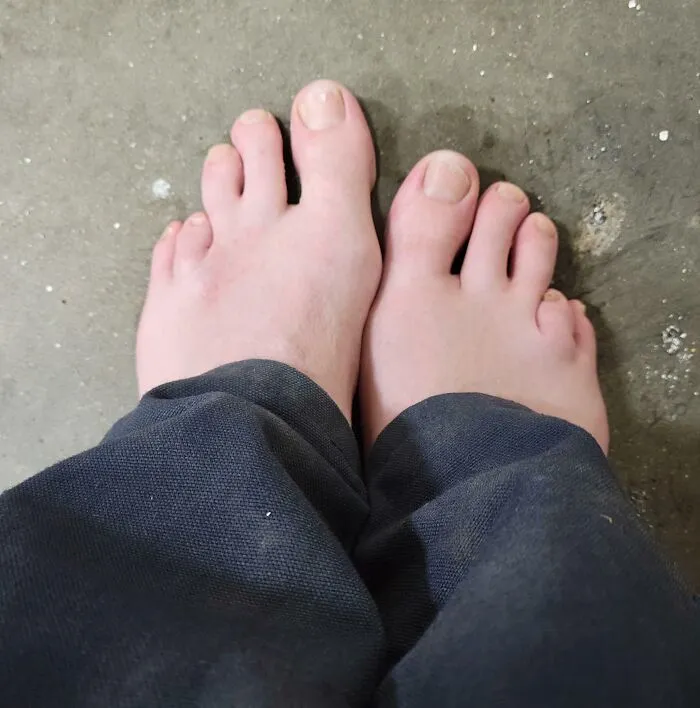 Overhead view of two bare feet with widely spread toes resting on a grey floor surface, showcasing human anatomy.