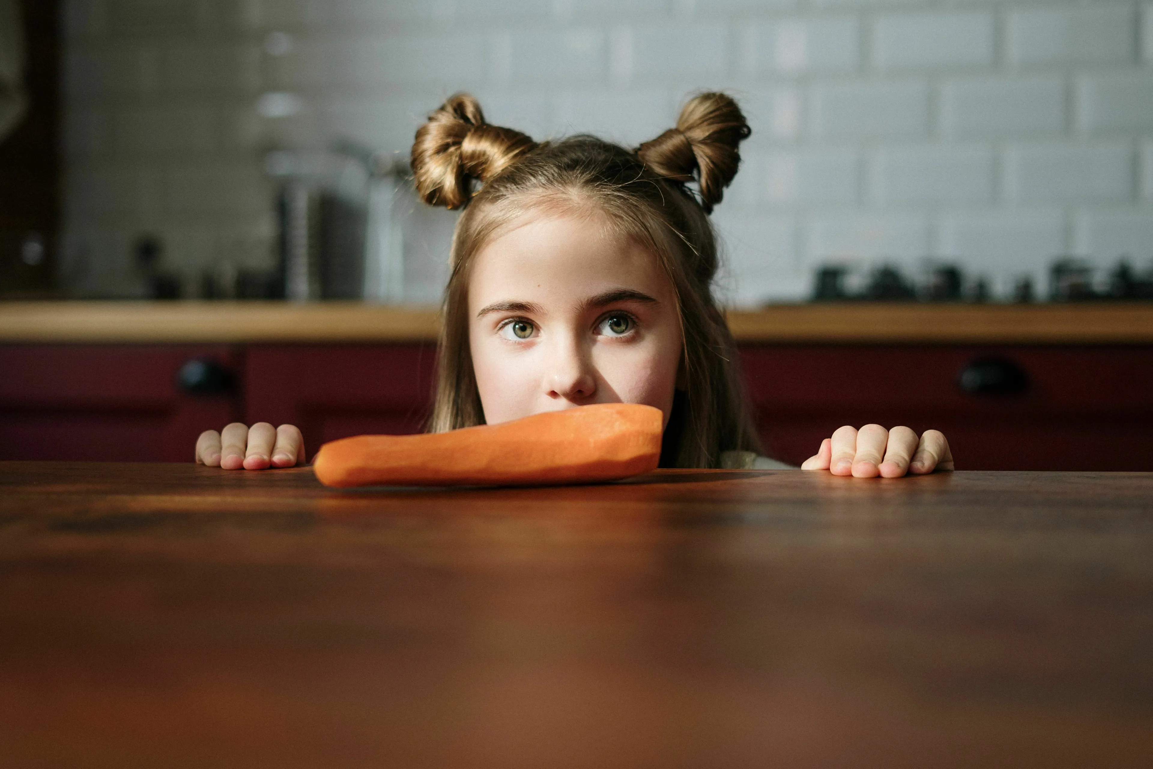 A young girl looking at a carrot, illustrating vitamin sources.