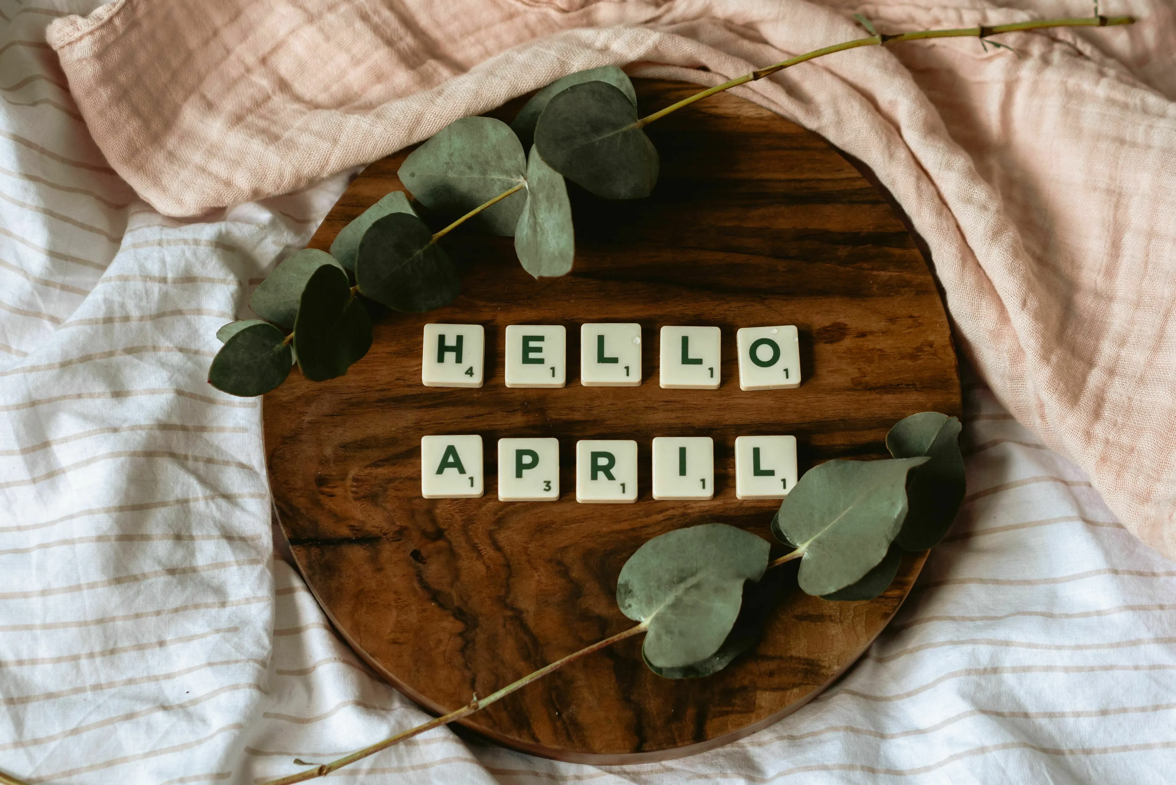 Scrabble letters spelling out Hello April on a wooden board, referring to the month of April.