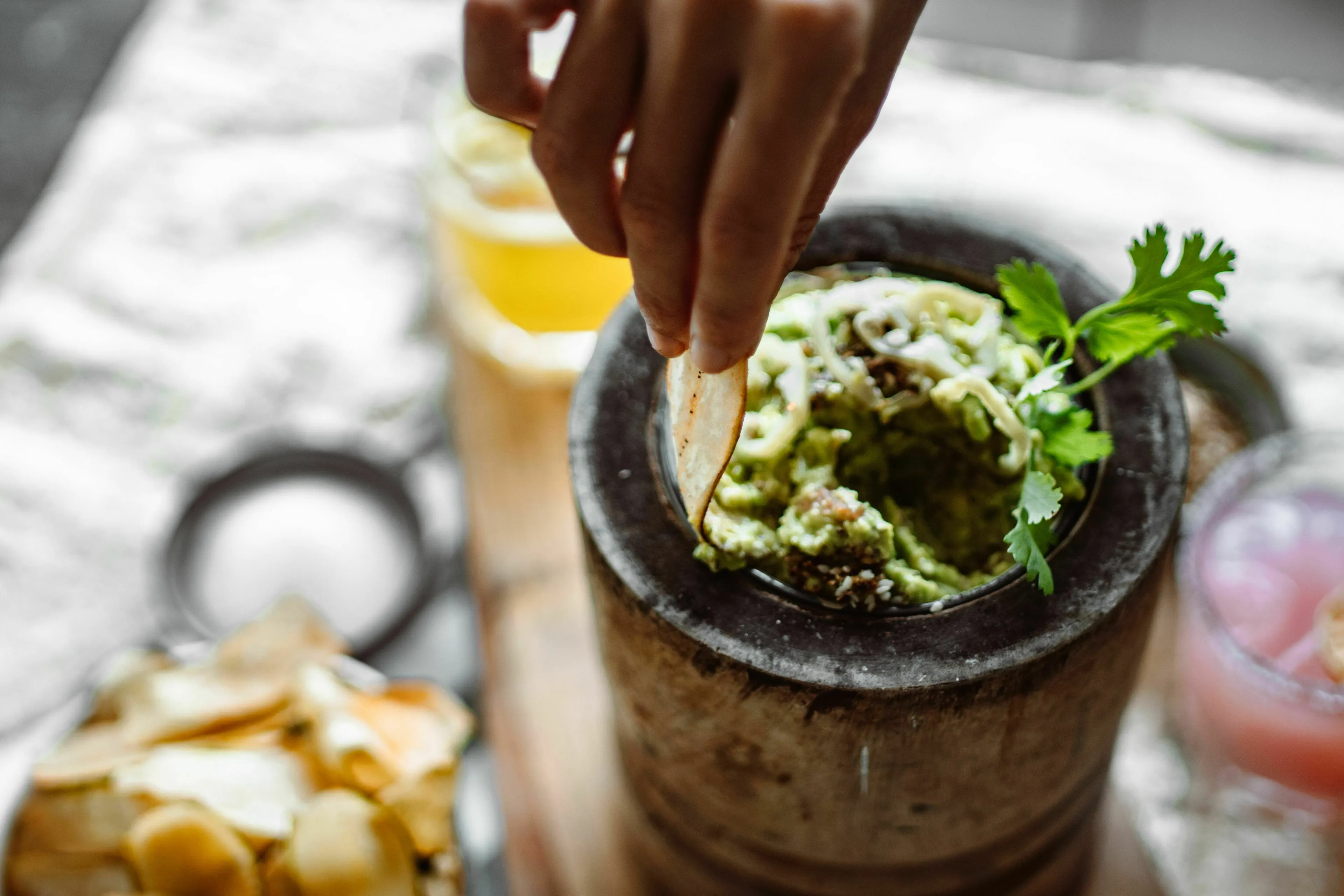 A hand dipping a tortilla chip into a fresh bowl of guacamole.