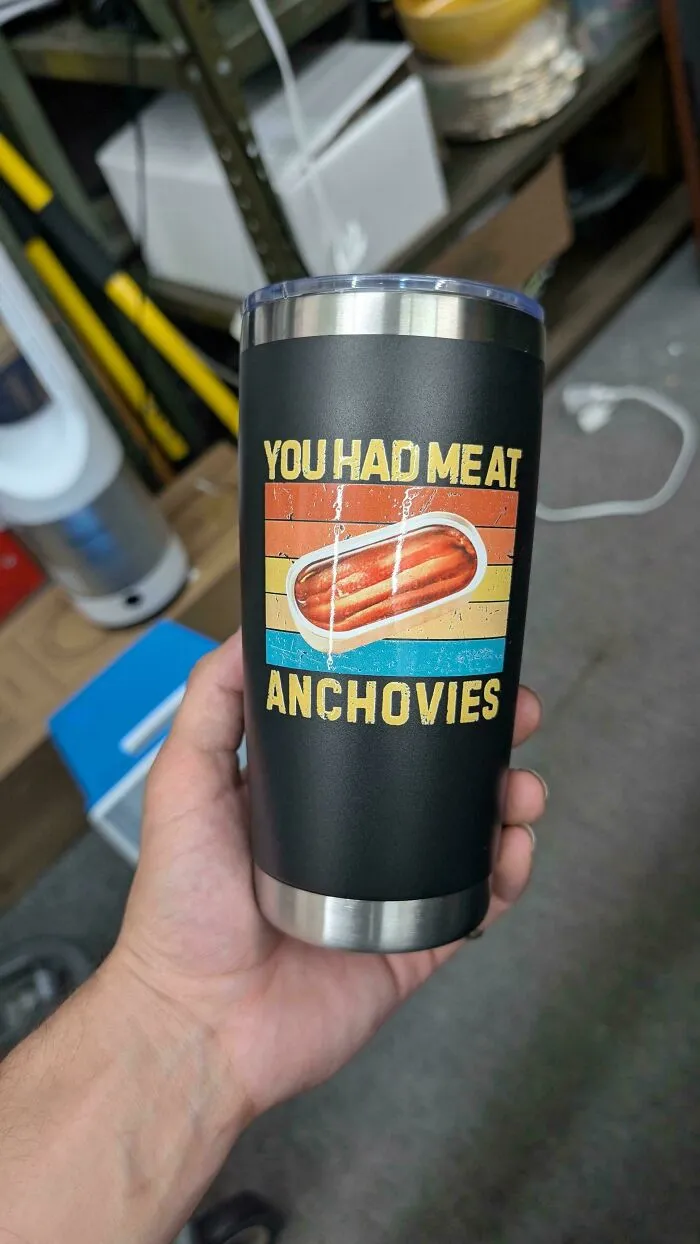 A black tumbler with a funny graphic and poor letter spacing reading You had meat anchovies.