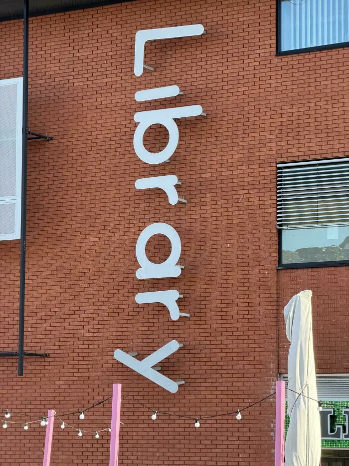 A brick wall displaying vertical library signage with terrible letter spacing.