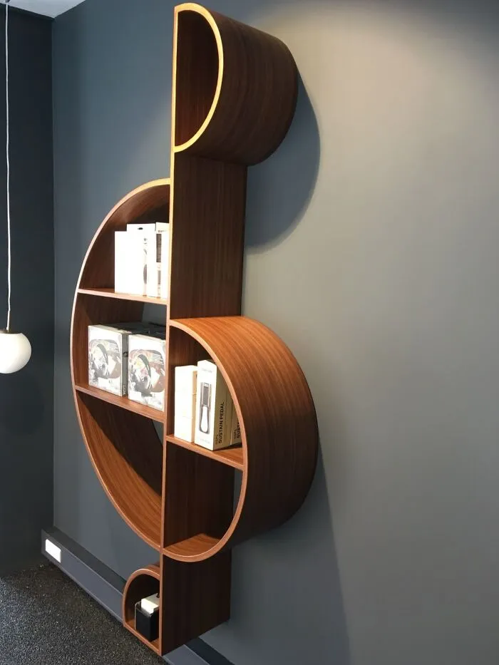 Clever wooden creations showing a music treble clef bookshelf mounted on a gray wall