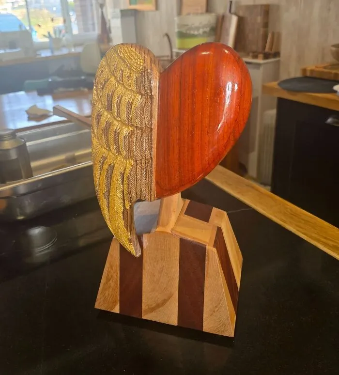 A handcarved heart with a golden wing, displaying unique wooden creations.