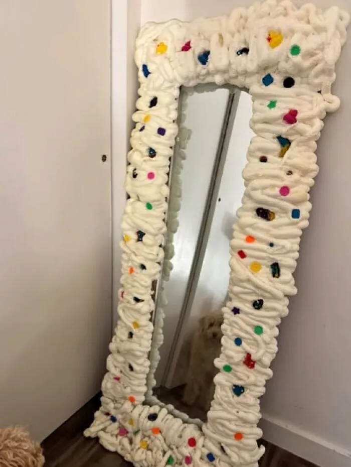 An odd craft project showing a full-length mirror surrounded by a messy foam frame.