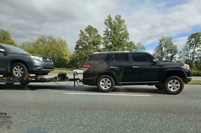 A black SUV towing another SUV on a trailer, showcasing questionable decisions on the highway.