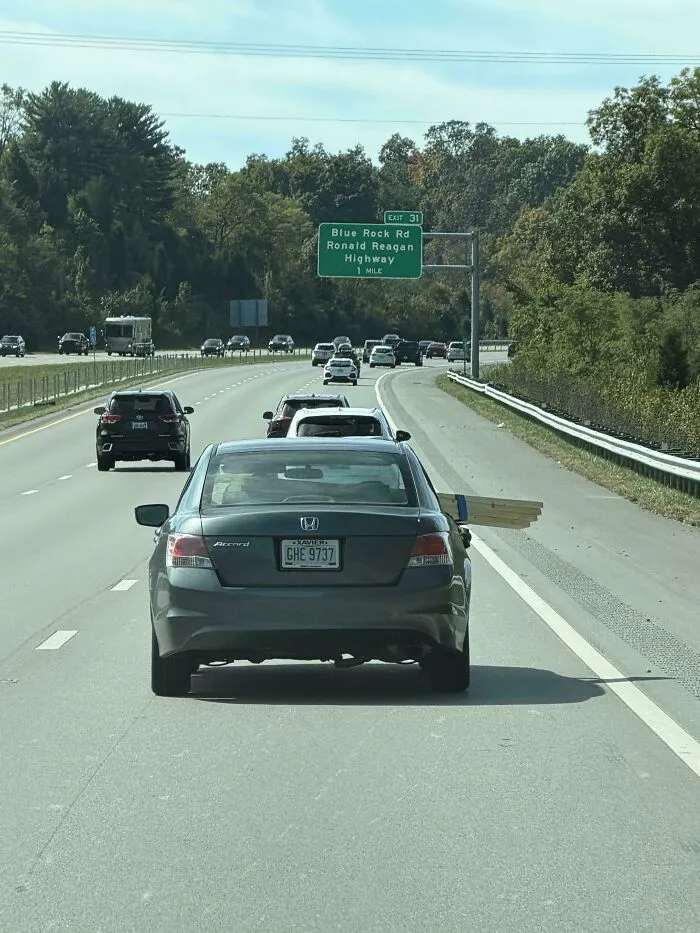 A sedan carrying long wooden planks sticking far out of the side window, demonstrating questionable decisions.