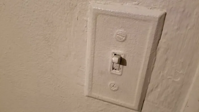 A light switch painted over completely with thick white paint illustrating questionable decisions in home DIY.