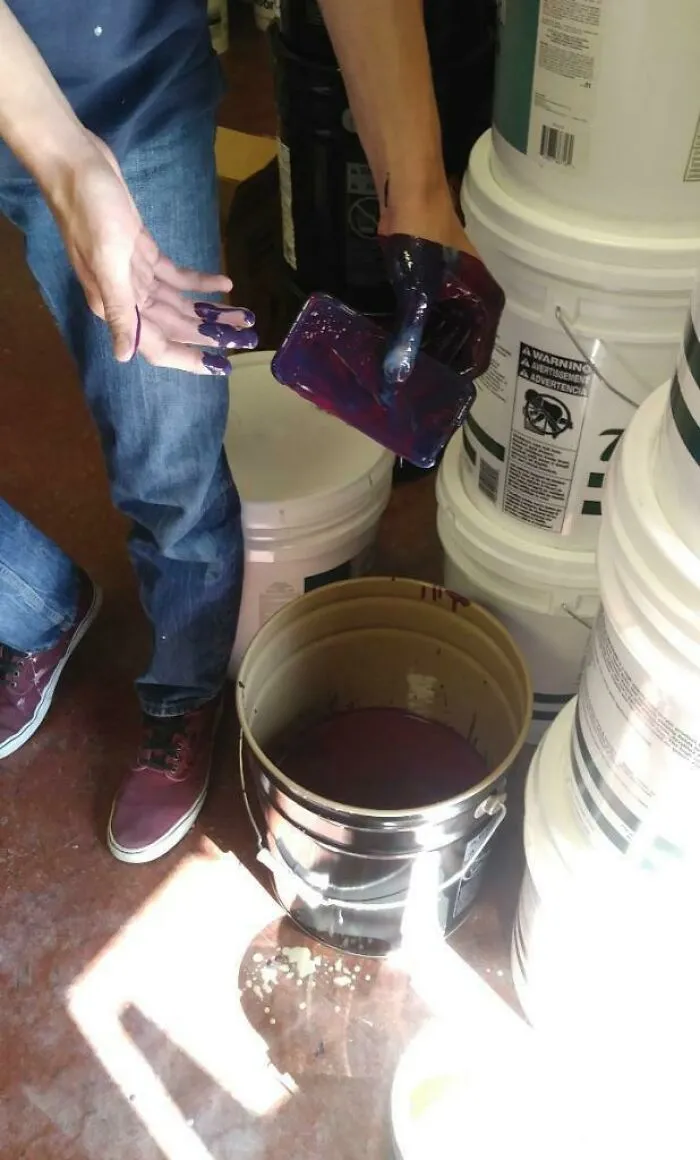 A questionable decision resulting in a smartphone covered in thick purple paint held above a paint bucket