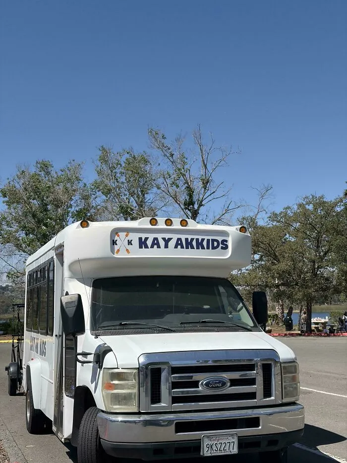 A white shuttle bus displaying a typography fail with awkward letter spacing for Kayak Kids