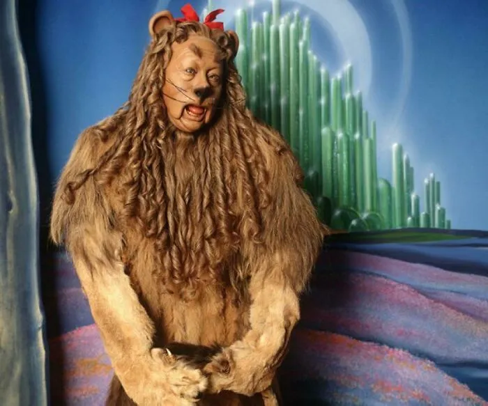 The Cowardly Lion costume displayed in front of the Emerald City background from movie props.