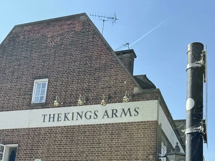 A brick pub building displaying one of several typography fails with THEKINGS ARMS painted on the side.