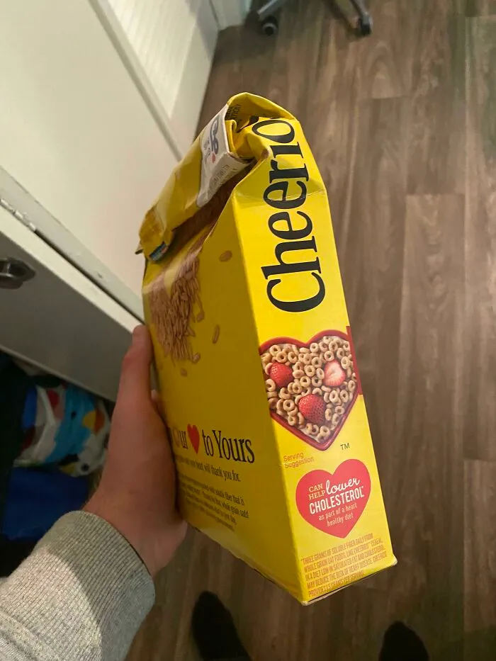 A hand holding a cereal box crushed from the side instead of open from the top, a questionable decision.