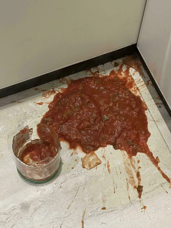 Spilled jar of red salsa pooled on the kitchen floor next to its broken glass container